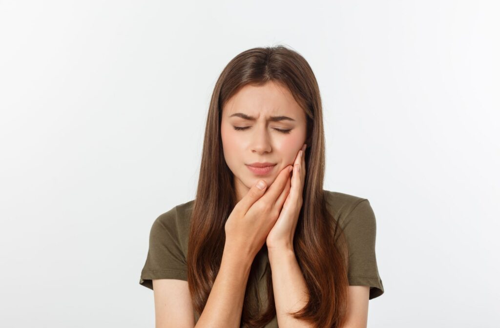 A woman holds the side of her jaw due to tooth pain.