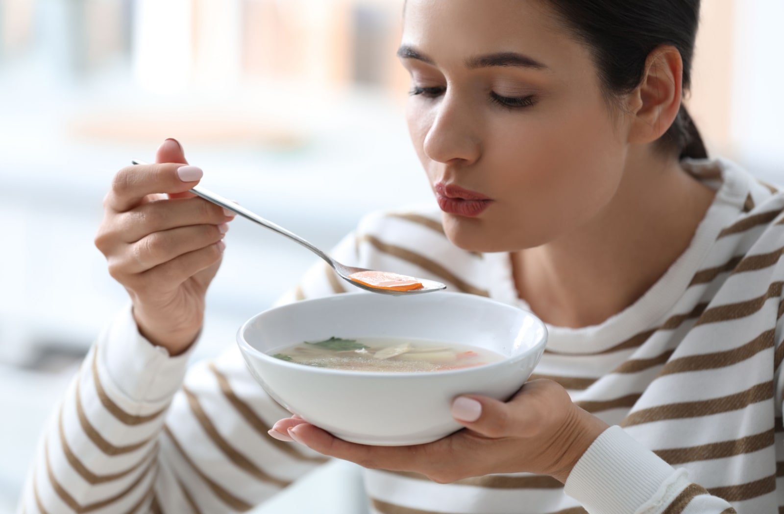 A young woman eating tasty vegetable soup after a root canal.