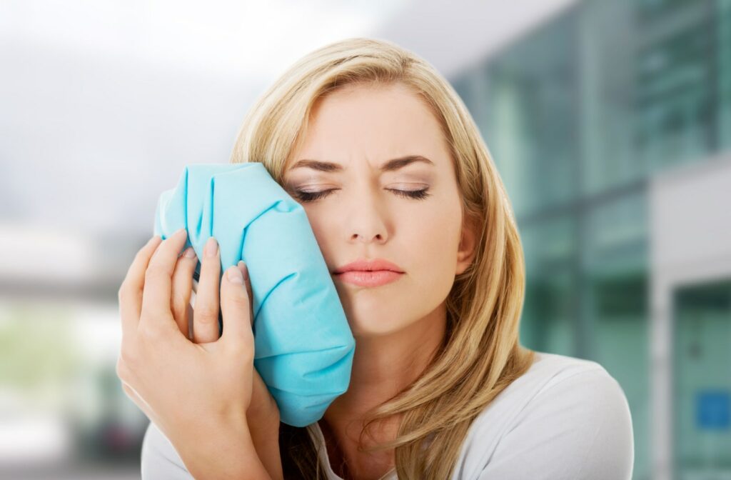 A woman holds a cold compress against her jaw due to tooth pain.